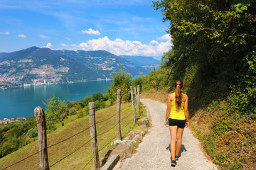 Female hiker go down and descent the pathway with spectacular landscape of Lake Iseo from Monte...