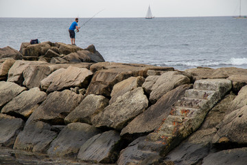 Fototapeta na wymiar Man fishing on rock wall in Newport RI