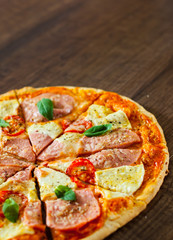 sliced Pizza with Mozzarella cheese, Ham, Tomatoes, pepper, Spices and Fresh Basil. Italian pizza on wooden background