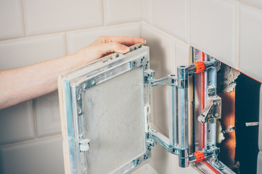 The girl opens a hidden hatch on the wall of the tile to access the inspection hole of the sewer pipe to eliminate clogging and cleaning - Powered by Adobe