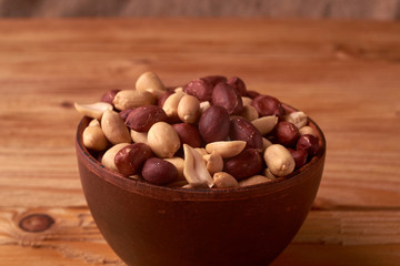 Deep fried peanuts in clay bowl over rustic wooden background. Selective focus