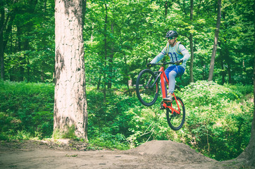 Naklejka premium Cyclist in helmet on an orange bike doing a trick in a springboard jump in the forest, motion blur