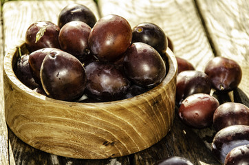 Vintage plums in a wooden bowl, on a wooden background, on the grass on a sunny afternoon on the grass.