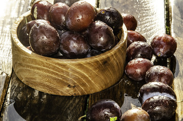 Fototapeta premium Vintage plums in a wooden bowl, on a wooden background, on the grass on a sunny afternoon on the grass.