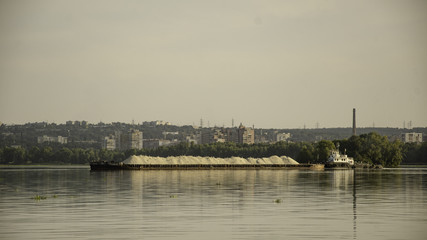 Obraz premium Barge with sand on the river, in the summer, against the backdrop of the city.