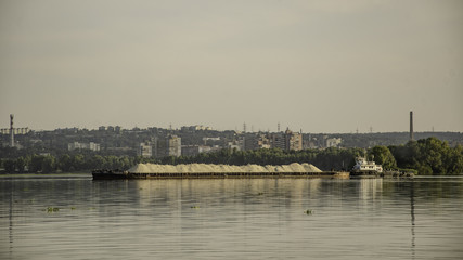 Obraz premium Barge with sand on the river, in the summer, against the backdrop of the city.