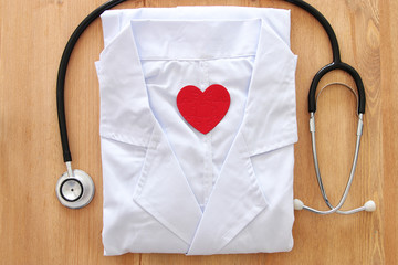 Image of stethoscope and doctor coat over wooden desk. Medical concept