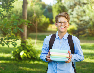 cute, young boy in round glasses in blue shirt with backpack holds books. Education, back to school concept 