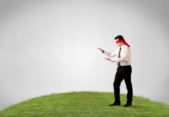 Young blindfolded businessman steps on a patch of grass