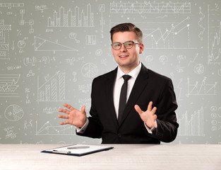 Young handsome businessman sitting at a desk with white graphs and calculations behind him 