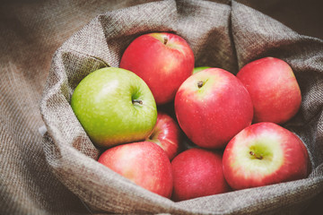 Red apples, green apple in the bowl cover with burlap, top view