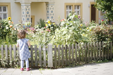 Mädchen steht vor Gartenzaun