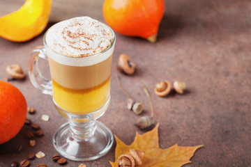 Pumpkin spiced latte or coffee in glass on brown background. Autumn, fall or winter hot drink.