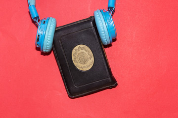 listen to quran concept, holy muslim book and bluetooth headphone  isolated on red background
