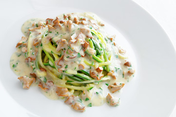 spaghetti made of zucchini under white sauce with chanterellas and parsley