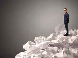 Thoughtful young businessman standing on a pile of crumpled paper with a deep grey background