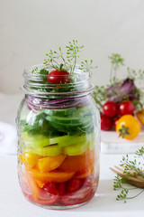 Fototapeta na wymiar Salad of vegetables with herbs in a glass jar and fresh vegetables on a table.