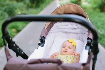 Cute little baby girl in yellow dress in brown baby carriage in the park, evening sun shine
