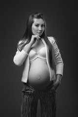 Fashionable pregnant woman with long healthy hair in stylish clothes on a dark studio background. Carefully embraces his belly