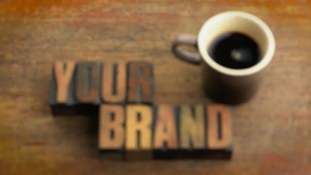 Your brand - rack focus on words in vintage letterpress wood type printing blocks (inverted) against grange wooden board with a cup of coffee