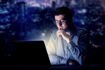 Young handsome businessman working late at night in the office with blue lights in the background