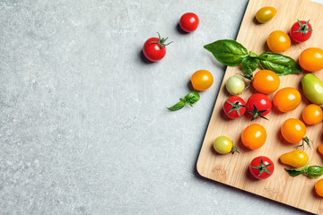 Wooden board with juicy tomatoes and space for text on grey background, top view