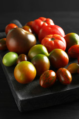 Wooden board with tasty tomatoes on table