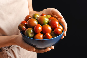 Woman holding bowl with tasty juicy tomatoes on black background, closeup