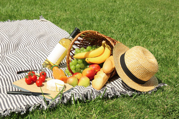 Basket with food and straw hat on blanket in park. Summer picnic
