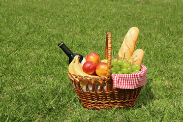 Basket with food and bottle of wine on lawn in park. Summer picnic