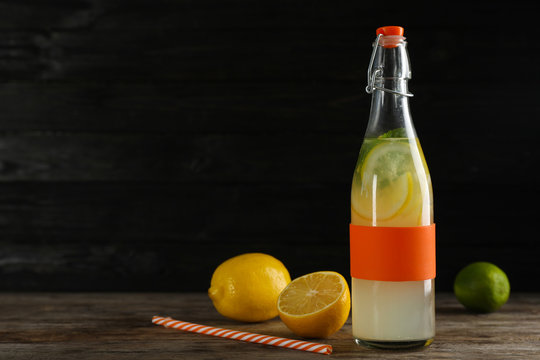 Bottle with natural lemonade on table against dark background