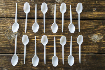 White plastic spoons on a wooden background.