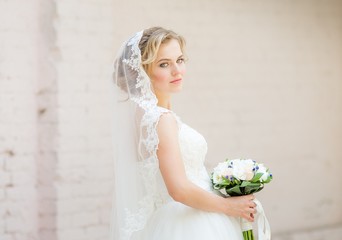Beautiful blonde bride with stylish make-up in white dress with a wedding bouquet