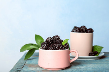 Fototapeta na wymiar Mug with fresh blackberry on table against color wall