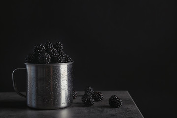Fototapeta na wymiar Mug with fresh blackberry on gray table against dark background. Space for text