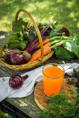 fresh vegetable beetroot onion carrots in a wicker basket and carrot juice in a glass cup on a wooden background in the garden, concept of organic organic gardening