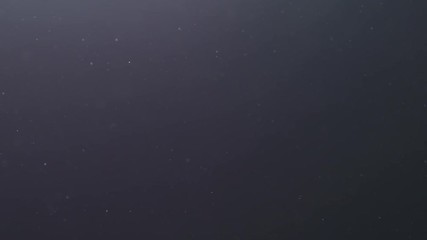 Slow motion backlit dust particles floating in the air on a black background with lens flare