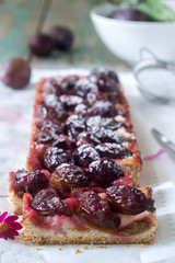 Sweet pie from short pastry with caramelized plums and ripe plums on a wooden table. Rustic style.