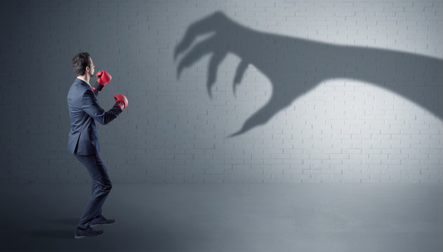 Tiny businessman fighting with scary hand shadow
