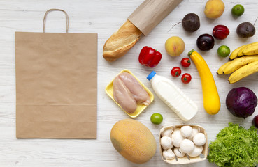 Variety of healthy food with paper bag on white wooden background. Flat lay of fresh fruits, veggies, greens, meat, milk. Top view, overhead, from above. Shopping groceries concept.
