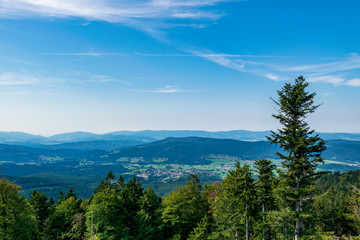 View from top of a mountain in the valley with clouds on the sky and mountains on the background and stones and trees in front of in the bavarian forest