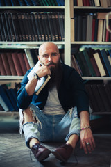 Bored stylish hipster man sitting on floor in library