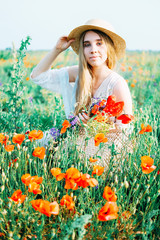 Young countryside girl sitting in the field of poppies