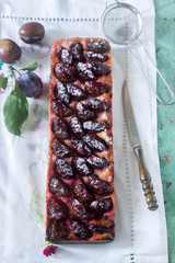 Sweet pie from short pastry with caramelized plums and ripe plums on a wooden table. Rustic style.