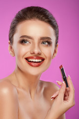 Beautiful woman, lipstick in hand. Beauty face. Picture taken in the studio, pink background.