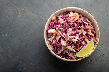 Purple cabbage and carrot salad with mayonnaise in a white bowl on a black background. Classic coleslaw. Diet vegetarian dish. Top view with copy space - obrazy, fototapety, plakaty