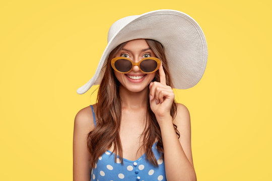 Delighed happy female dressed in summer clothes, enjoys good vacation in resort place, going on beach, smiles broadly, being in good mood, poses against yellow background. People and rest concept