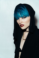 fashion photography of a girl with blue hair on a white background looking directly at the camera. Thick yellow chain and bijouterieher on her neck. Professional model posing in studio