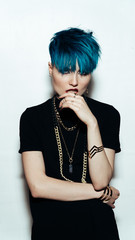 fashion photography of a girl with blue hair on a white background looking directly at the camera. Thick yellow chain and bijouterieher on her neck. Professional model posing in studio