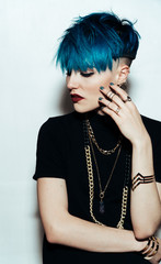 fashion photography of a girl with blue hair on a white background looking directly at the camera. Thick yellow chain and bijouterieher on her neck. Professional model posing in studio